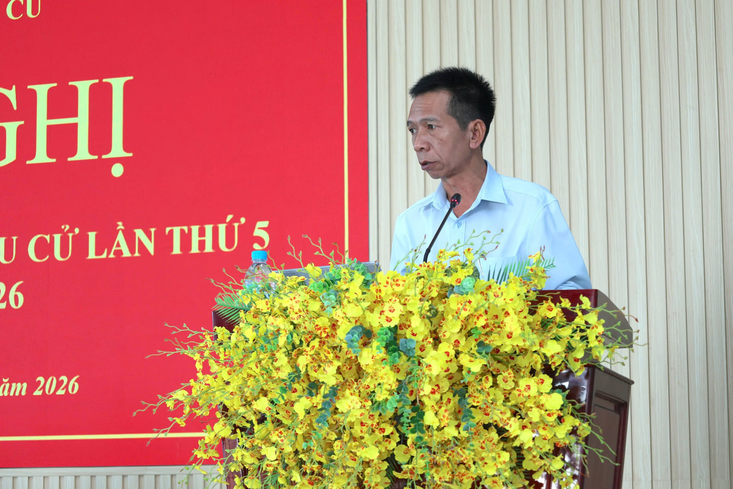 'A person standing at a podium with yellow flowers

Description automatically generated'