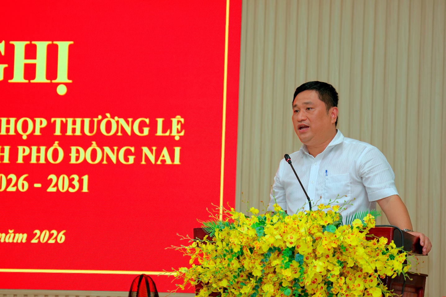 'A person standing at a podium with yellow flowers

Description automatically generated'