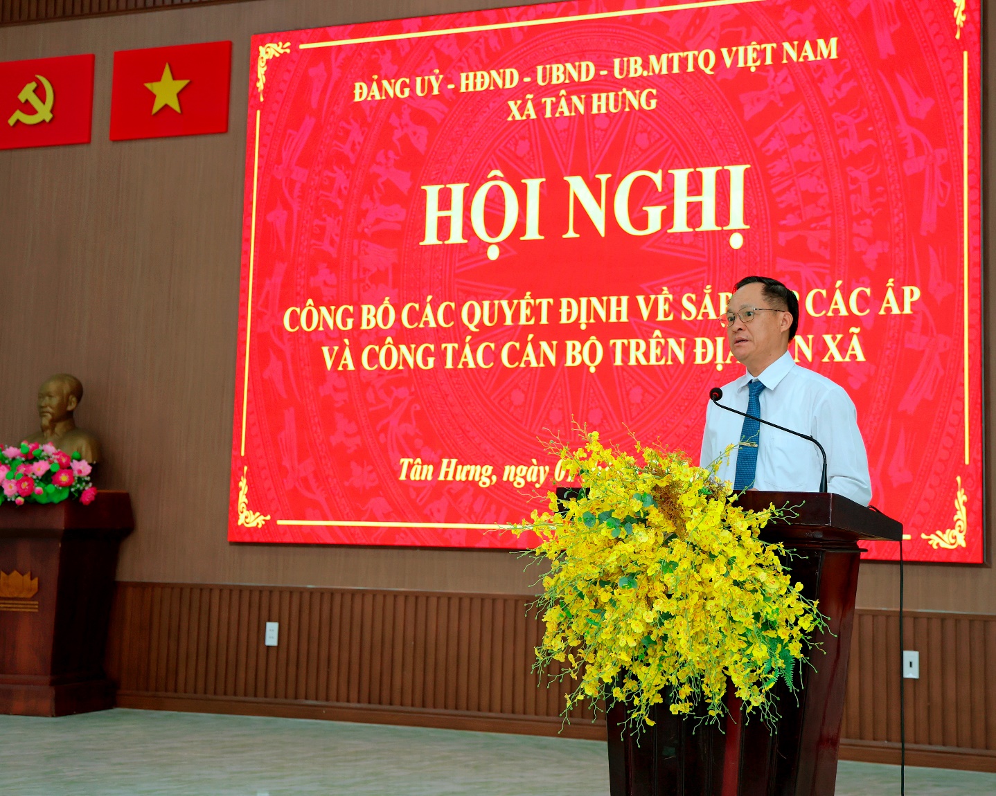 'A person standing at a podium with a large screen behind him

Description automatically generated'